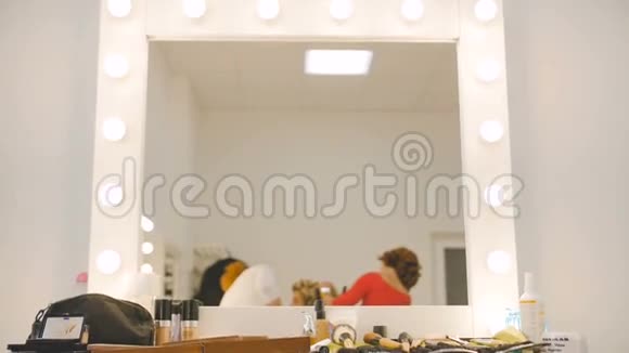 化妆师和理发师在慢动作工作室沙龙为金发模特做准备的镜像视频的预览图