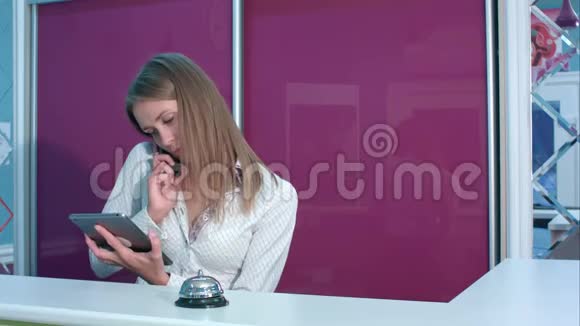 忙碌的女接待员在酒店大堂柜台后拿着平板电脑打电话视频的预览图