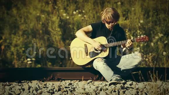 在阳光明媚的日子里金发的吉他手坐在铁路上演奏视频的预览图