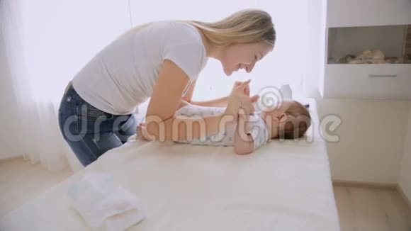 年轻有爱心的母亲和躺在换洗桌子上的小男孩聊天玩耍视频的预览图
