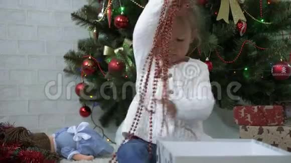可爱的小女孩在装饰圣诞树附近玩礼盒和花环视频的预览图
