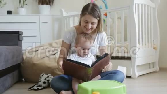 快乐的年轻母亲和她的小儿子坐在客厅的地板上在大书里给他看照片视频的预览图
