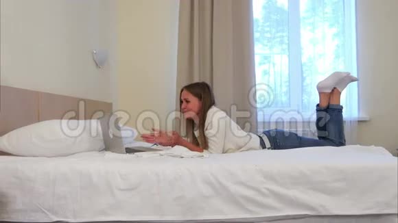 幸福的女人躺在酒店的床上通过笔记本电脑进行视频通话视频的预览图