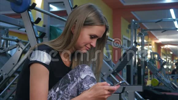年轻女子在健身房休息手机上发短信视频的预览图