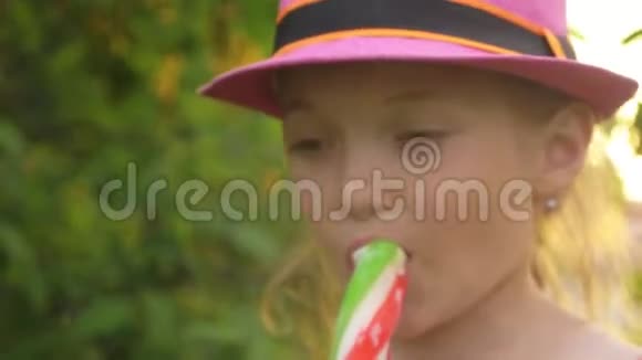 戴帽子的孩子舔冰淇淋女孩正在吃美味的奶油冰淇淋用草莓棒涂成五颜六色的冰淇淋视频的预览图