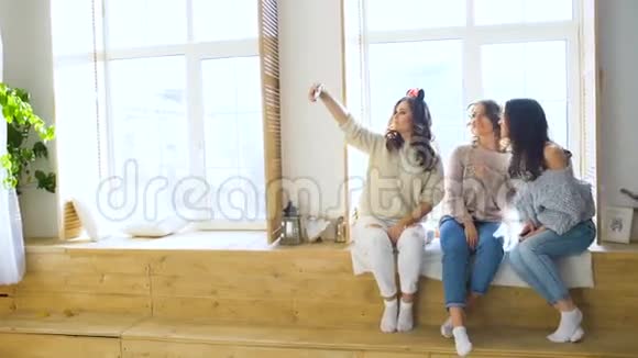 三个漂亮的女孩坐在窗户上自拍女朋友在卧室里开怀大笑视频的预览图