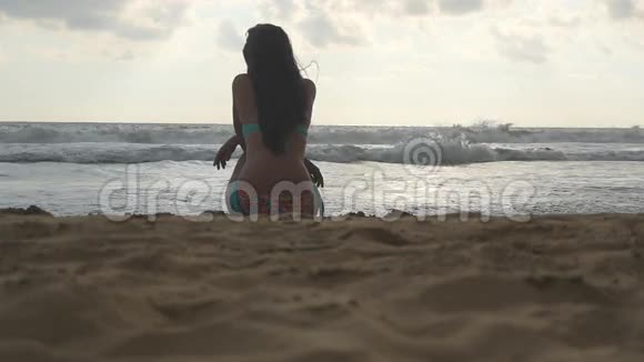 穿比基尼的年轻女孩坐在沙滩上望着大海美丽的女人看着日落视频的预览图