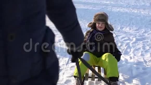 爸爸把他的儿子卷在雪橇上男孩开心地笑着寒冷的晴天慢动作视频的预览图