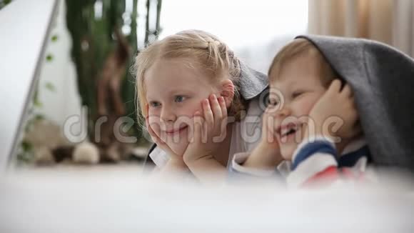 现代儿童生活中的计算机弟弟和妹妹在笔记本电脑上看动画片躺在床上视频的预览图