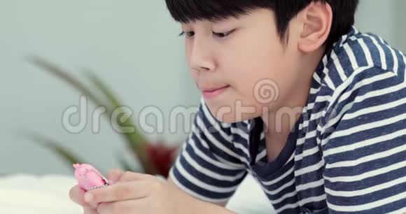带着智能手机短信或在家玩游戏的亚洲微笑男孩视频的预览图
