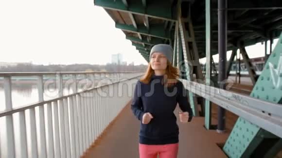 年轻女跑步者在工业桥上慢跑的慢动作视频的预览图