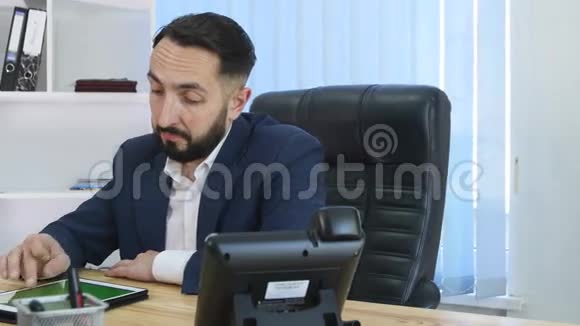 年轻英俊的胡子男在现代的创业办公室里使用触摸屏平板电脑视频的预览图