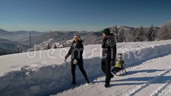 年轻的幸福家庭在雪林里玩得很开心父母把他们的小儿子卷在雪橇上慢动作视频的预览图