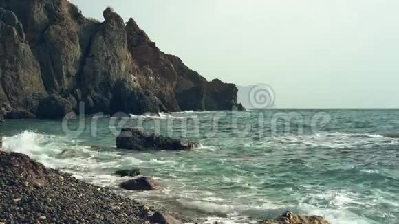 波浪冲刷卵石滩波浪再次拍打着一片荒凉的海滩背景上有古老山脉的海景视频的预览图
