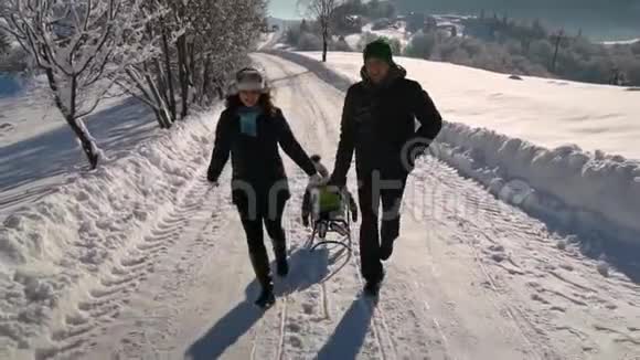 年轻的幸福家庭在雪林里玩得很开心父母把他们的小儿子卷在雪橇上慢动作视频的预览图