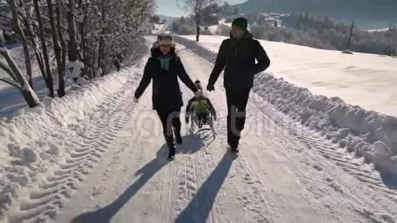 年轻的幸福家庭在雪林里玩得很开心父母把他们的小儿子卷在雪橇上慢动作视频的预览图