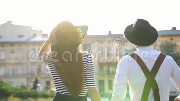 戴着黑帽子的迷人男人和女人在夕阳下沿着街道散步视频的预览图