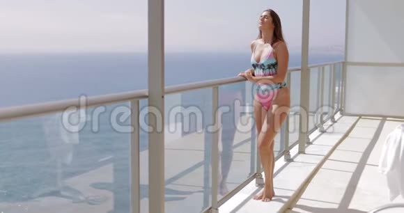 穿着泳装在阳台上摆姿势的内容女士视频的预览图