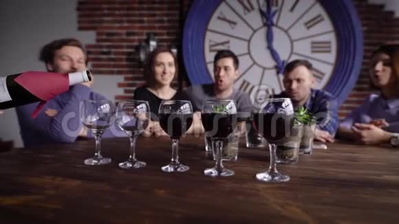 为坐在后台的一群朋友在杯子上倒红酒的侍酒师的特写镜头视频的预览图