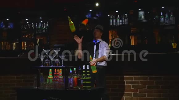 杂技表演由巴曼杂耍两个瓶子和烧杯进行混合酒吧背景慢动作视频的预览图