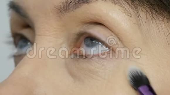 化妆师用高光遮瑕膏给蓝眼睛的中年妇女化妆年龄化妆特写肖像视频的预览图
