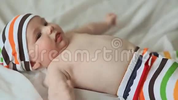 有趣的四个月大的婴儿躺在他的背上微笑穿着条纹短裤和帽子的婴儿视频的预览图