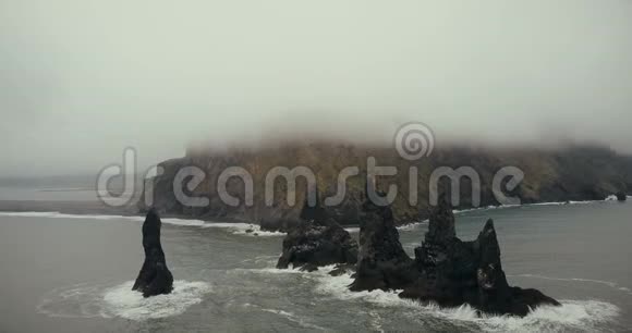 冰岛黑色火山海滩和巨魔脚趾悬崖的空中景观背景上的山被白雾覆盖视频的预览图