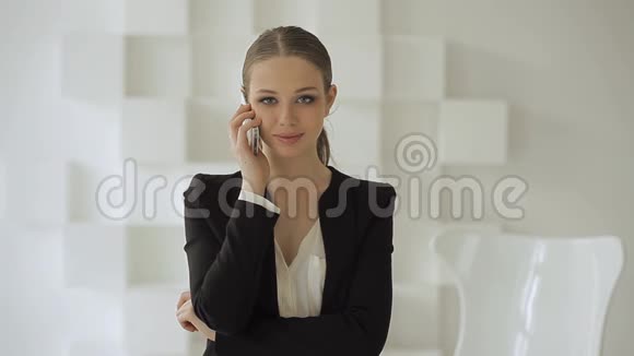 年轻的商务女性站在一张白色椅子附近的手机上微笑着在一间白色的办公室里视频的预览图