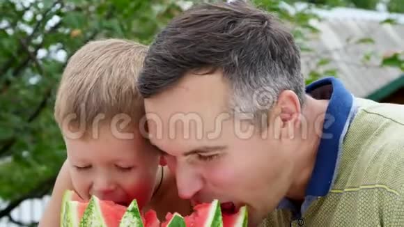 夏天在花园里爸爸和一个四岁的儿子切了一个西瓜吃了它玩得开心一个男孩喜欢西瓜视频的预览图