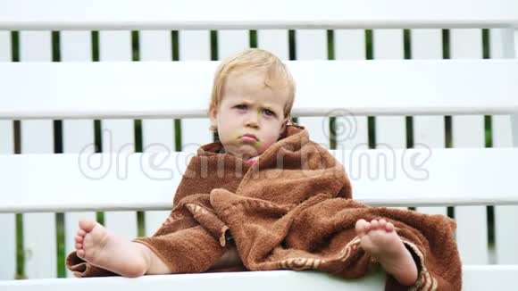 一个一岁的小女孩裹着毛巾脸很脏孤独地坐在花园里的秋千上在花园里视频的预览图