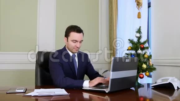 一位心情愉快的商人在办公室里用笔记本电脑工作视频的预览图