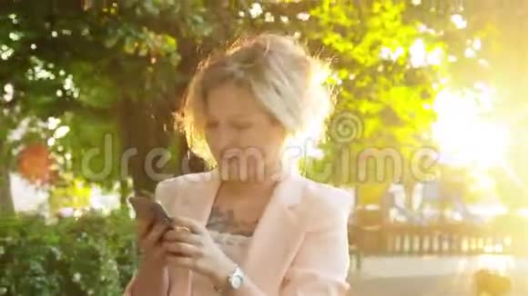 迷人的年轻女子在公园散步使用智能手机视频的预览图