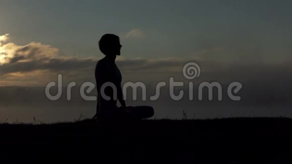 金发男人坐在湖岸上在日落慢动作练习瑜伽视频的预览图