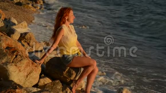 坐在亚得里亚海多岩石的海滩上头发飞扬的年轻女子视频的预览图