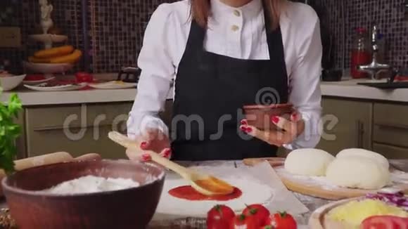 女人在厨房里做披萨的时候在面团上放酱汁视频的预览图