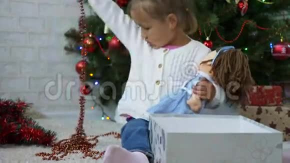 可爱的小女孩在礼品盒附近玩花环装饰圣诞树视频的预览图