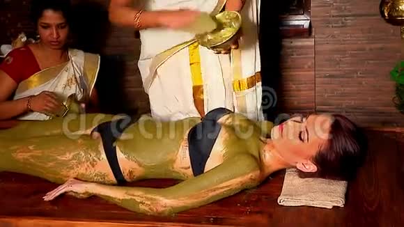 印度女性美容师将天然的治疗粘土应用于病人的身体视频的预览图