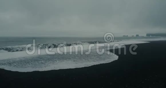 冰岛美丽的黑色火山海滩的鸟瞰图在阴天带着泡沫的海浪在海岸上涌来视频的预览图