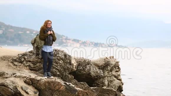 一个背着背包的女旅行者站在海上的岩石上视频的预览图
