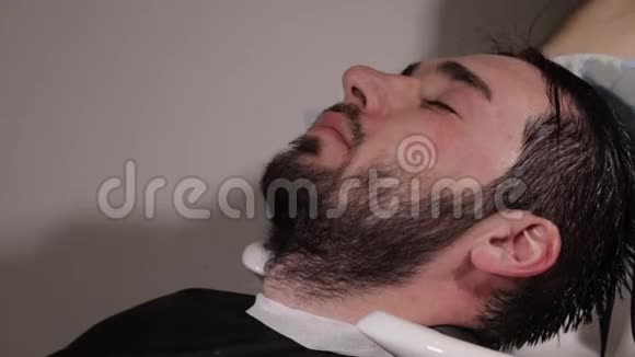理发师在理发店里洗黑发男子的头发视频的预览图