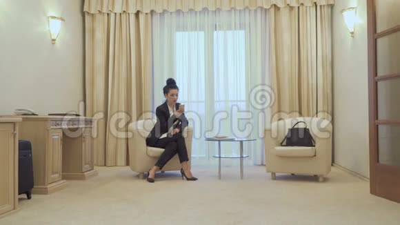 穿着黑色西装的漂亮女人坐在酒店房间里打电话视频的预览图