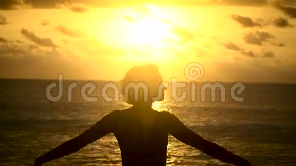 小女孩一头短发穿着一件T恤在靠近大海的黄色夕阳下举起双手视频的预览图