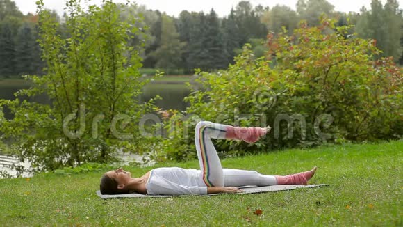 年轻女子屈膝躺在河岸的瑜伽垫上视频的预览图