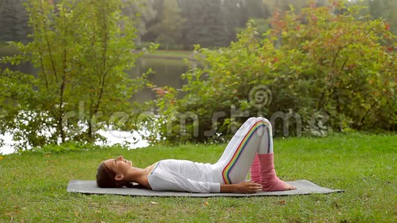 年轻女子在河岸躺在瑜伽垫上训练双手视频的预览图