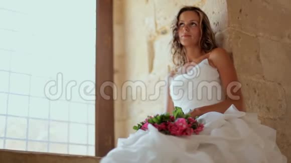 一位美丽的新娘坐在老城堡的窗户附近视频的预览图