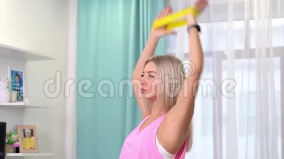 美丽的女人在时尚运动服装制作与黄色乐队在家锻炼家庭概念训练视频的预览图