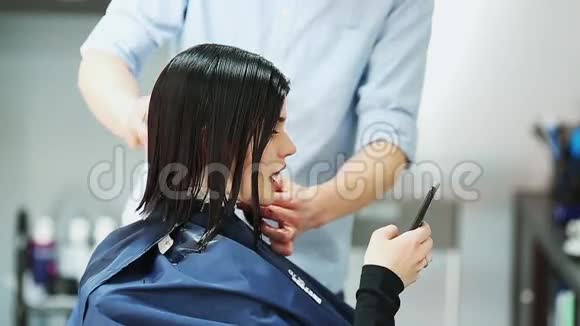 理发店里漂亮的女孩客户美女坐在镜子前穿着蓝色的裙子拿着手机视频的预览图