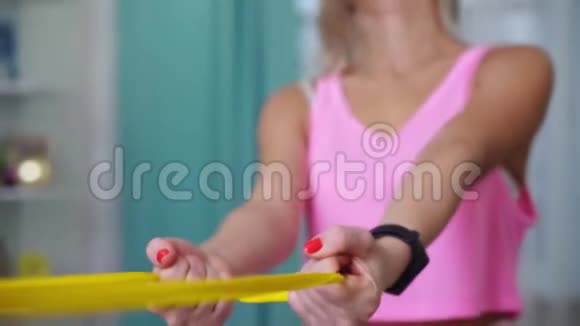 美丽的女人在时尚运动服装制作与黄色乐队在家锻炼家庭概念训练视频的预览图
