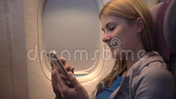 飞机窗户附近美丽迷人的女人长途飞行使用智能手机浏览视频的预览图