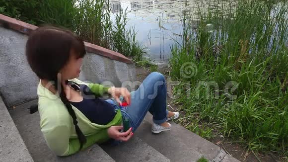美丽的女孩在城市公园里吹泡泡机靠近湖边和芦苇视频的预览图